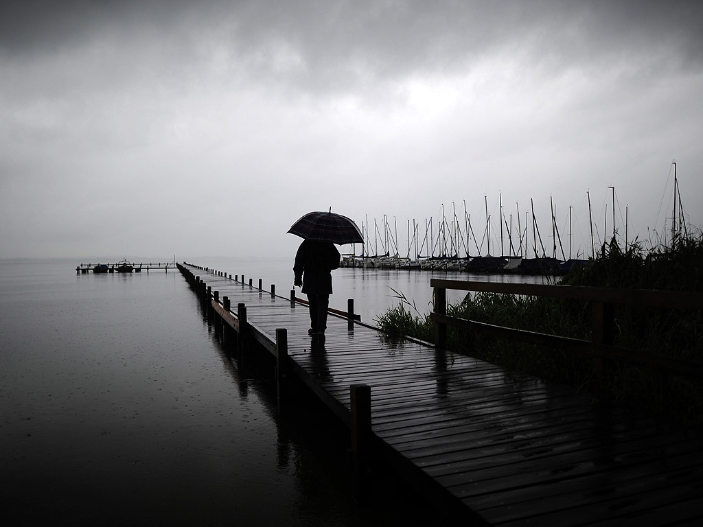 Човек се разхожда с чадър на кея на езеро в Германия.