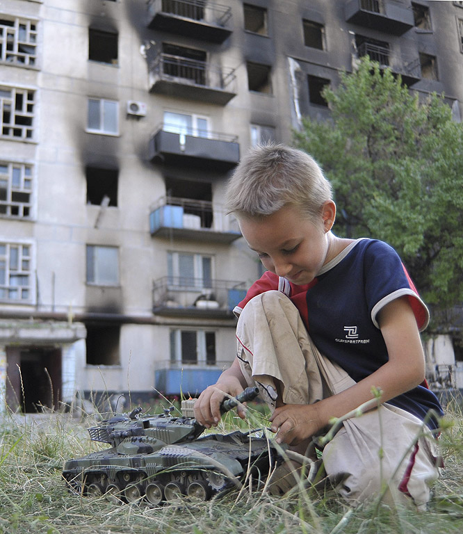 Дете с играчка танк пред разрушена сграда в Лисичанск, район близо до Луганск