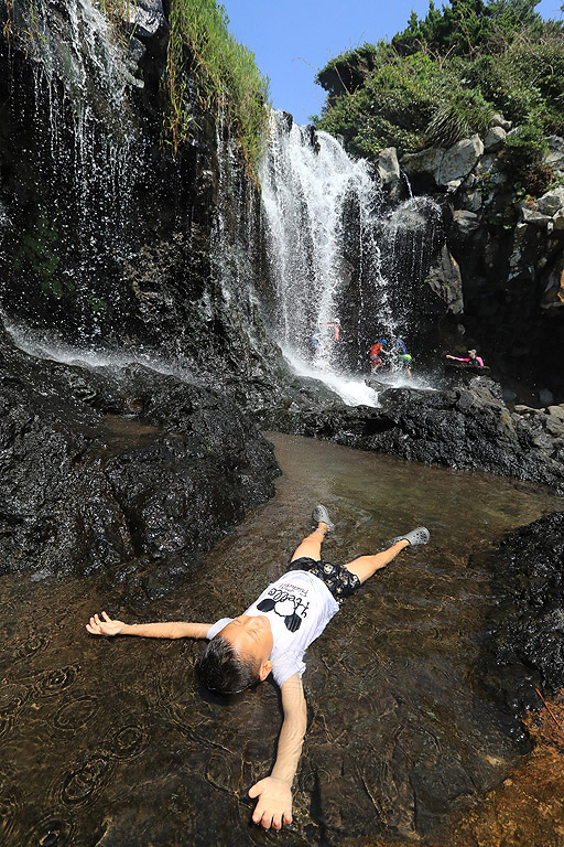 Дете е открило уютно място, за да се охлади от жегата в един водопад в Сеогвипо, Южна Корея