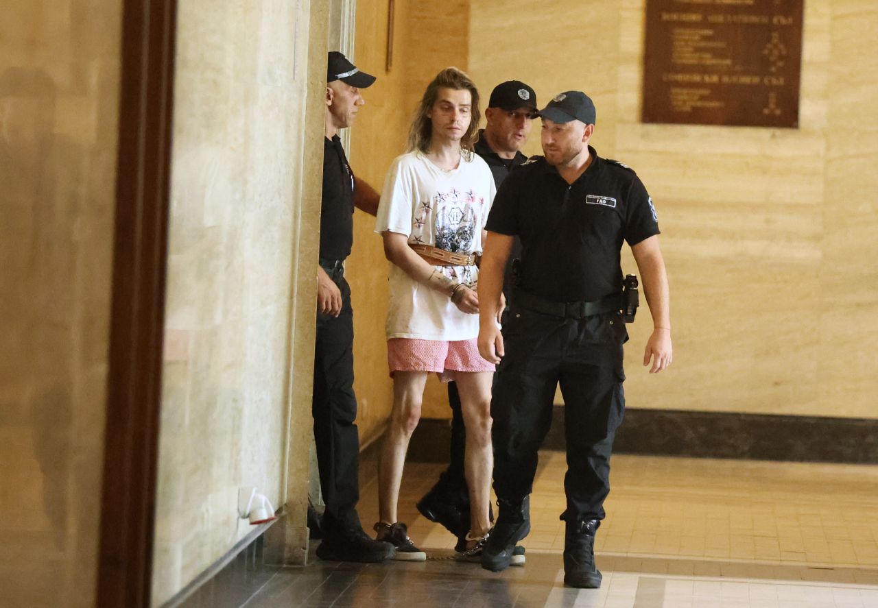 <p>Окован в белезници и пранги на краката, украинецът Ярослав Гуляткин бе доведен под засилен конвой в Съдебната палата. Задържаният за убийство на жена в София направи впечатление с татуировките по лицето и нетипичното си облекло по време на делото за мярката му.</p>