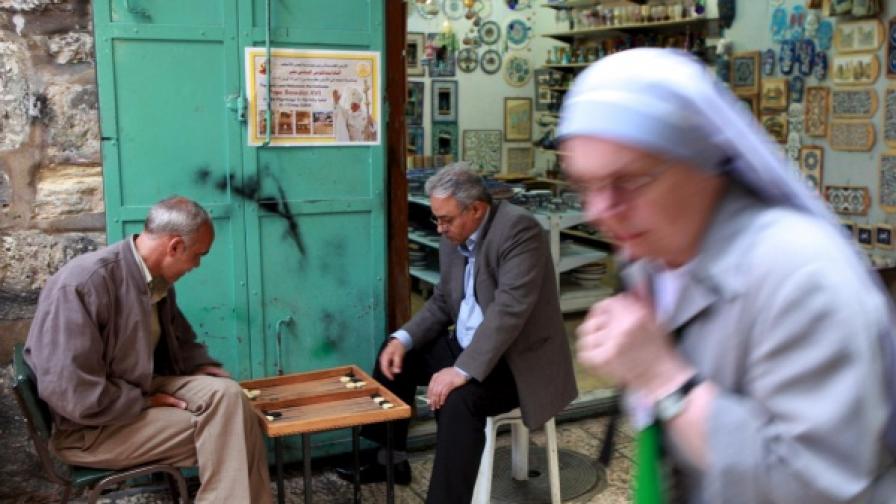 Християнска монахиня минава край палестинци, които играят табла на улицата под плакат за посещението на папата в Стария град в Ерусалим